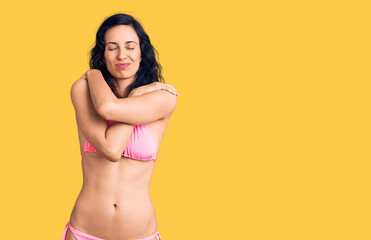 Young beautiful hispanic woman wearing bikini hugging oneself happy and positive, smiling confident. self love and self care