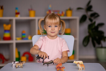 child girl playing with toys animals at the table in kindergarten or at home