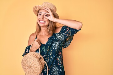 Middle age hispanic woman wearing summer hat holding wicker bag smiling happy doing ok sign with...