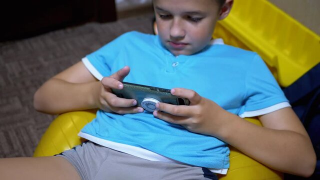 Smiling Boy Sit Plays a Mobile Game on Smartphone at Home in Relaxed State