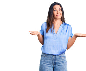 Young beautiful brunette woman wearing casual t-shirt clueless and confused expression with arms and hands raised. doubt concept.