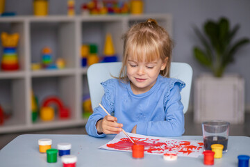 Cute little girl draws with paints in kindergarten