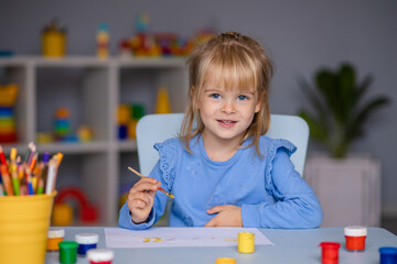 Cute little girl draws with paints in kindergarten