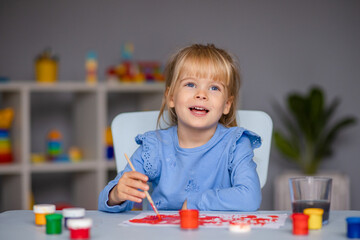 Cute little girl draws with paints in kindergarten