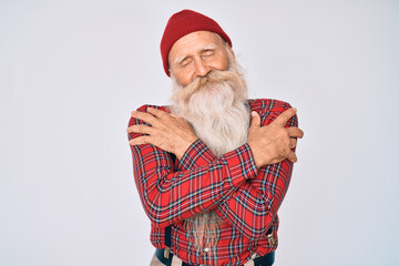 Old senior man with grey hair and long beard wearing hipster look with wool cap hugging oneself...