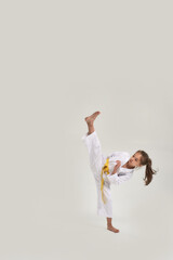 Full length shot of little karate girl in white kimono with a yellow sash exercising and fighting, doing martial arts, standing isolated over white background