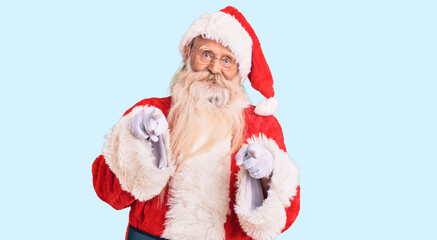 Old senior man with grey hair and long beard wearing traditional santa claus costume pointing fingers to camera with happy and funny face. good energy and vibes.