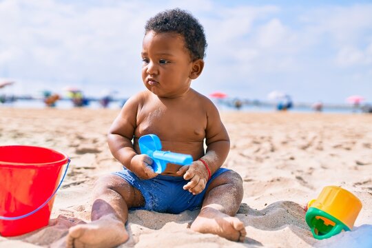 Adorable african american toddler playing with toys sitting on the sand at the beach.