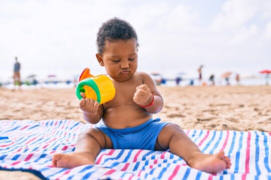 Adorable african american toddler playing with toys sitting on the sand at the beach.