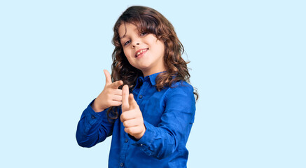Cute child with long hair wearing casual clothes pointing fingers to camera with happy and funny face. good energy and vibes.