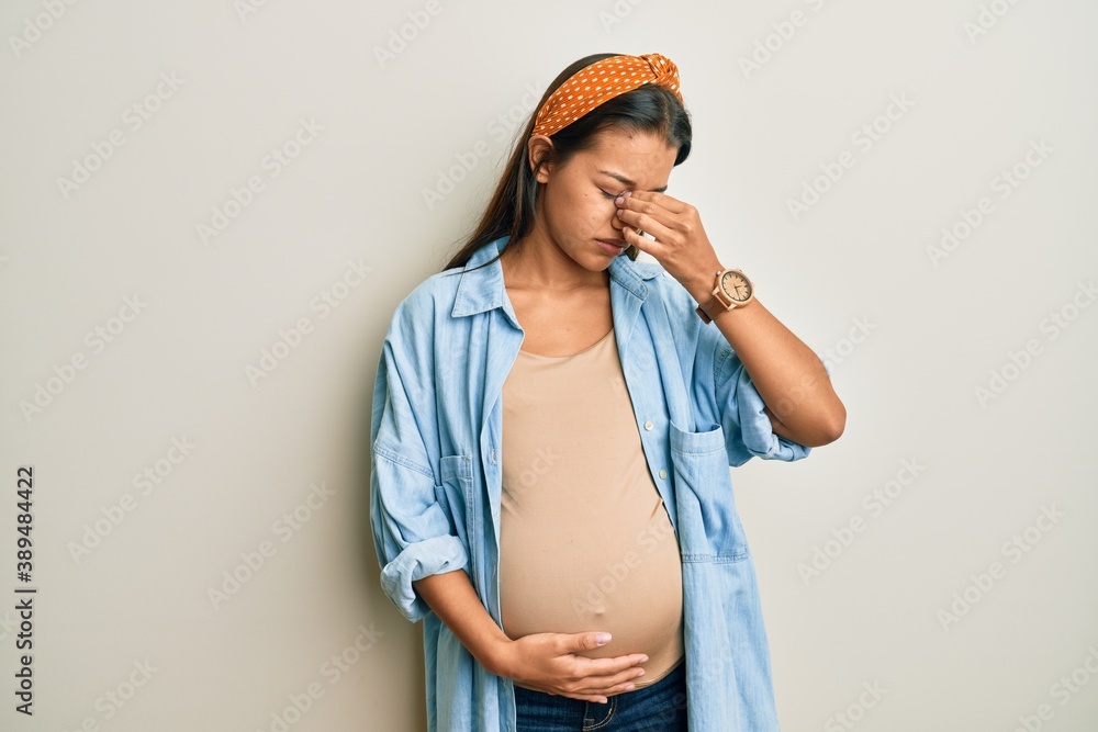 Sticker Beautiful hispanic woman expecting a baby, touching pregnant belly tired rubbing nose and eyes feeling fatigue and headache. stress and frustration concept.