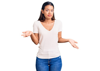 Young beautiful latin girl wearing casual white t shirt clueless and confused expression with arms and hands raised. doubt concept.