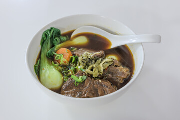 Selected focus view at Taiwanese stew Beef Noodle Soup without noodle in white bowl on white table.