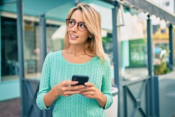 Young blonde woman smiling happy using smartphone at the city.