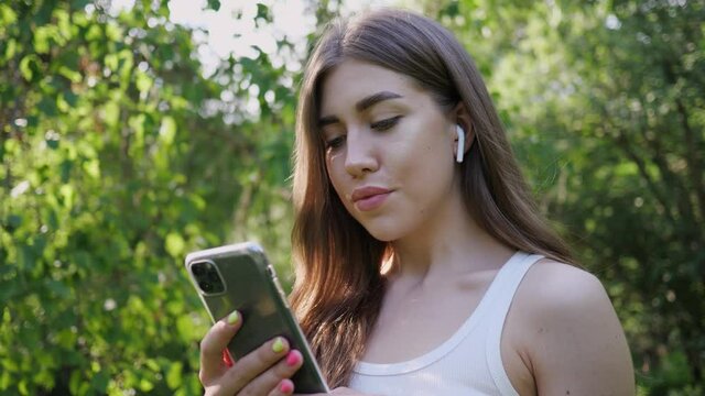 portrait young beautiful woman listening music in wireless earphone from phone