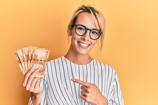 Beautiful blonde woman holding south african 20 rand banknotes smiling happy pointing with hand and finger