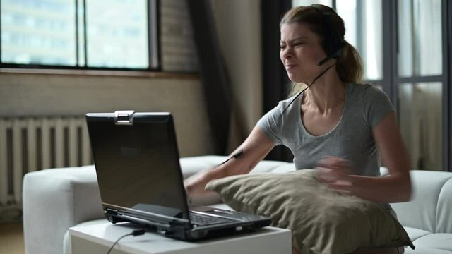 A young woman gets annoyed and angry at a slow old laptop and throws it off the table in anger. Old technology is annoying with its slowness