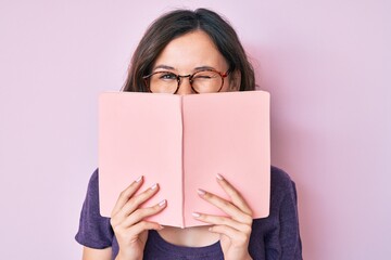 Young beautiful woman wearing glasses reading book winking looking at the camera with sexy...