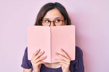Young beautiful woman wearing glasses reading book smiling looking to the side and staring away...