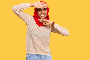 Young african american woman wearing traditional islamic hijab scarf smiling cheerful playing peek a boo with hands showing face. surprised and exited