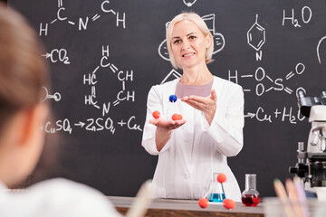 Smiling teacher of chemistry presenting model of molecule of chemical compound
