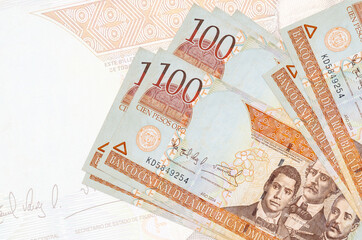 100 Dominican peso bills lies in stack on background of big semi-transparent banknote. Abstract...
