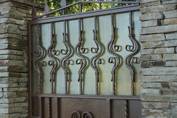 a part of a brown metal wall with a forged pattern and a fragment of a gray stone fence on the...
