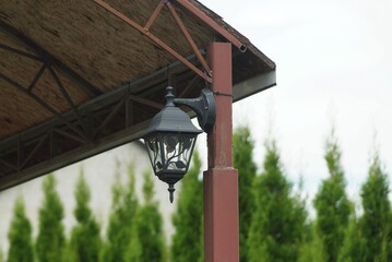 one black metal lantern hangs on a brown iron pole of an open veranda outside against the sky