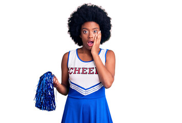 Young african american woman wearing cheerleader uniform holding pompom afraid and shocked,...