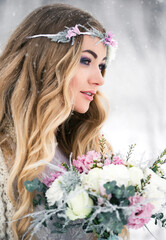 Cute bride in the winter snow forest outdoors with beautiful flowers on her head and a bouquet.