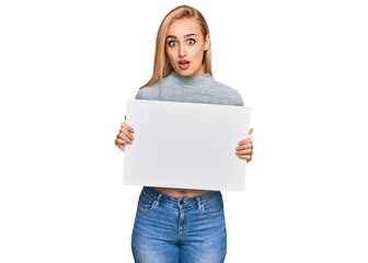 Fototapeta premium Beautiful caucasian woman holding blank empty banner scared and amazed with open mouth for surprise, disbelief face