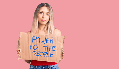 Young beautiful blonde woman holding power to the people banner thinking attitude and sober expression looking self confident