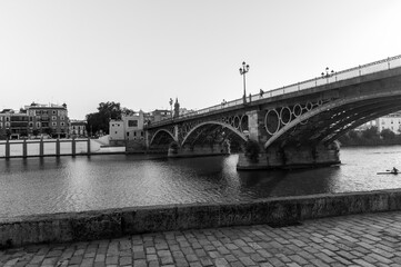 Fototapeta na wymiar Black and white photograph of the Isabel II Bridge better known as the Triana Bridge which connects the Triana neighborhood and the city center of Seville (Andalusia, Spain).
