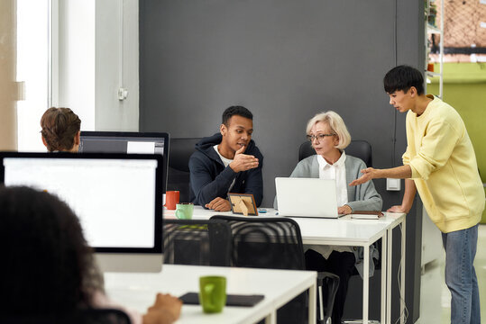 Friendly male workers training or teaching new employee, Young men explaining tasks to aged woman, senior intern while preparing her for first day at work