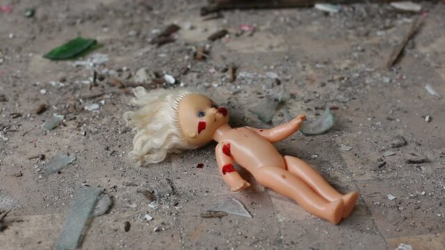 Childish doll covered in blood. Blood drips onto the doll. A baby doll lies in an abandoned building and is covered in blood.