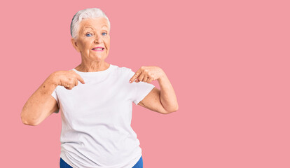 Senior beautiful woman with blue eyes and grey hair wearing casual white tshirt looking confident with smile on face, pointing oneself with fingers proud and happy.