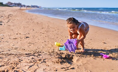 Adorable blonde child wearing bikini. Building sand castle using bucket and shovel at the beach