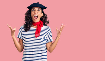 Middle age beautiful woman wearing french beret and scarf crazy and mad shouting and yelling with aggressive expression and arms raised. frustration concept.