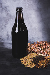 Unlabeled bottle of dark beer accompanied by malted barley seeds and coffee