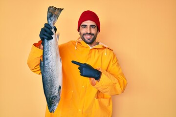 Handsome hispanic man with beard wearing fisherman equipment smiling happy pointing with hand and...