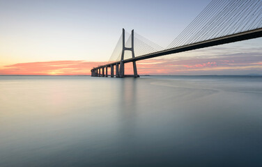 Background with colourful sunrise on the Lisbon bridge. The Vasco da Gama Bridge is a landmark, and one of the longest bridges in the world. Urban landscape. 