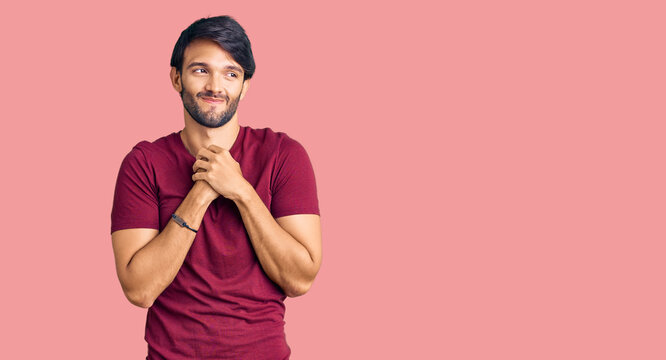Handsome hispanic man wearing casual clothes laughing nervous and excited with hands on chin looking to the side