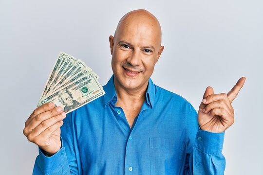 Middle age bald man holding 20 dollars banknote smiling happy pointing with hand and finger to the side