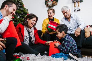 Latin kids opening Christmas gifts surrounded by extended senior mexican family
