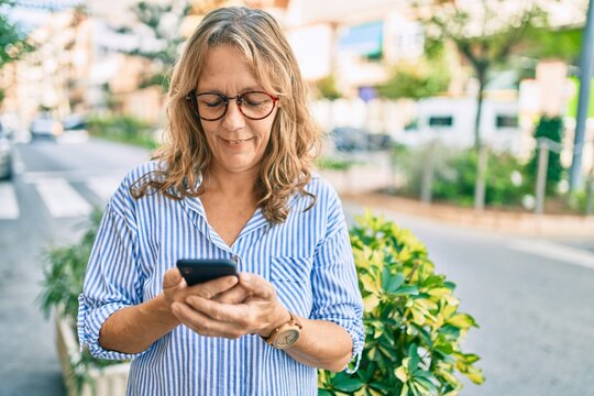 Middle age caucasian woman smiling happy using smartphone at the city.