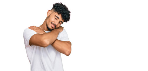 Young arab man wearing casual white t shirt hugging oneself happy and positive, smiling confident. self love and self care