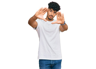 Young arab man wearing casual white t shirt doing frame using hands palms and fingers, camera perspective