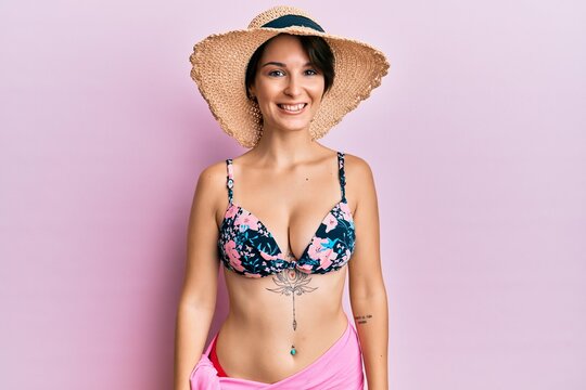 Young brunette woman with short hair wearing bikini and hat with a happy and cool smile on face. lucky person.