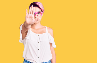 Young beautiful woman with pink hair wearing casual clothes and glasses doing stop sing with palm of the hand. warning expression with negative and serious gesture on the face.