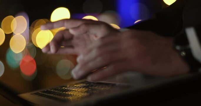 Close up, a man presses his fingers on the laptop keyboard keys against a background of blurry city lights
in boke. Nervously presses one button and spreads her fingers away from surprise.